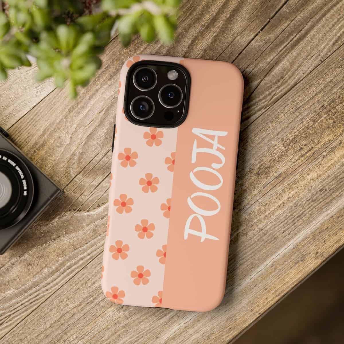 Pink floral phone case with POOKA inscription and camera accessories on wooden table.