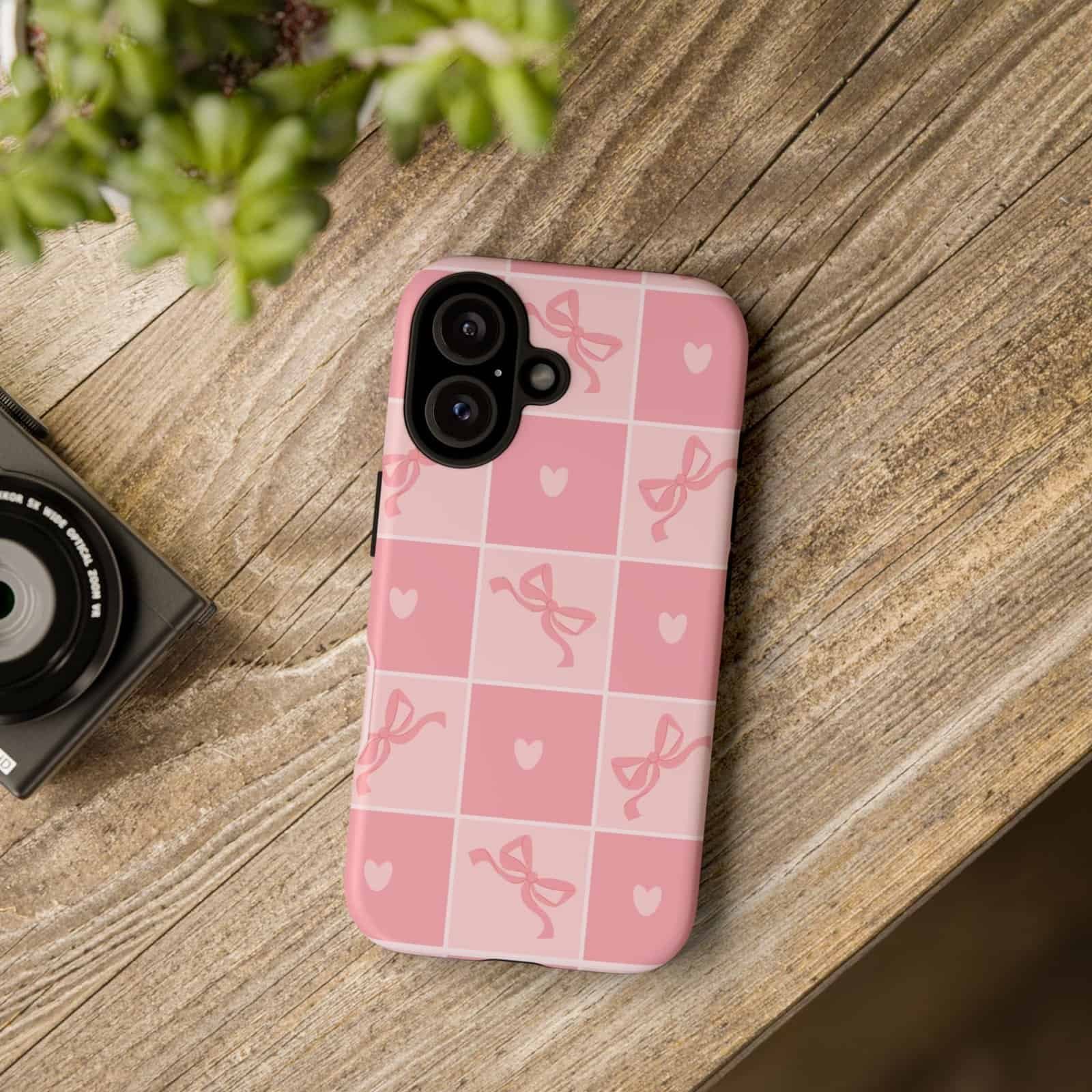 Pink checkered phone case with bows and hearts for iPhone, stylish accessory for mobile protection.